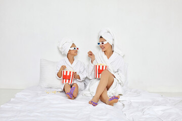 Obraz na płótnie Canvas woman with daughter in white bathrobes watching movie