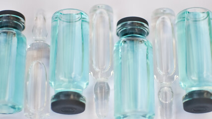 Vial vaccine, top view of glass ampoules with transparent and blue liquid lying on white background, global vaccination concept