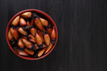 Typical araucaria seeds used as a condiment in Brazilian cuisine in winter. Brazilian pinion nuts in brown and red wooden bowl on gray wooden background