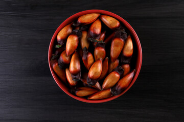 Typical araucaria seeds used as a condiment in Brazilian cuisine in winter. Brazilian pinion nuts in brown and red wooden bowl on gray wooden background
