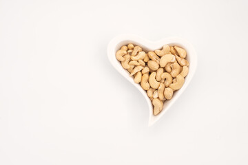 Cashew nuts heart shape plate. Isolated on white background.