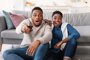 Excited black couple spending time together watching tv