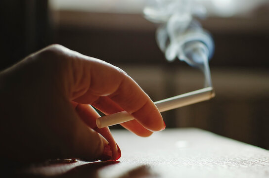 Hand holds a smoking cigarette. Smoking harm concept.