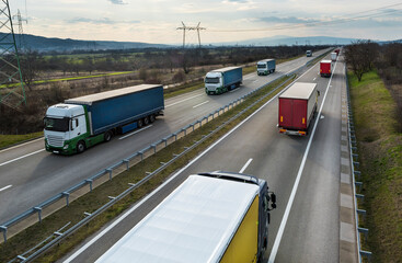 Convoys or caravans of transportation trucks passing on a highway on a bright blue day. Highway transit transportation with white and red lorry trucks
