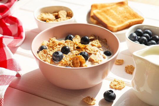 Breakfast of whole wheat flakes with milk, blueberries and toast close-up on wooden table. Selective focus, morning concept