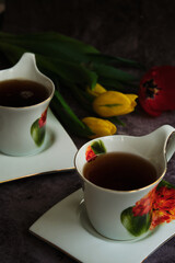 two white cups of tea and yellow and red tulips