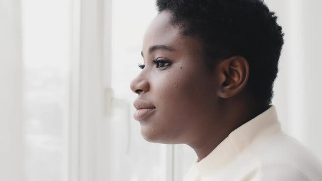 Portrait of afro american woman ethnic lady millennial black girl african model looking out window standing in daylight dreaming thinking contemplating turns female face head looking at camera smiling