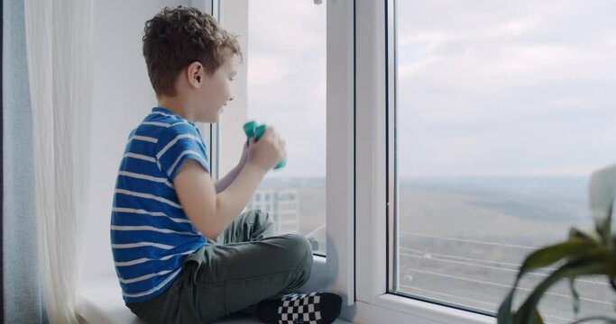 A small boy looks with binoculars at the window at home. Sun day.