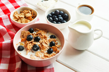 Tasty breakfast of whole wheat flakes with milk, blueberries and cup of coffee close-up on wooden table. Healthy food. Selective focus