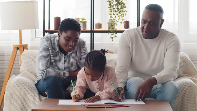 Afro american family three 3 generations adult mother woman older sister with little girl daughter schoolgirl granddaughter pupil and mature grandfather man drawing home schooling help with homework