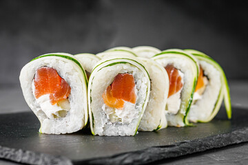 appetizing green sushi roll with philadelphia cheese cucumber and salmon on a black stone plate