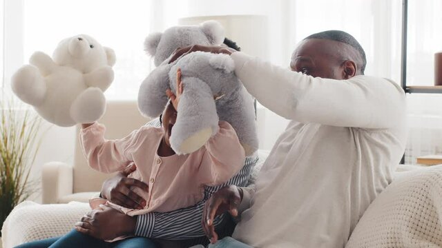 Family portrait african american family three generations adult mother woman, little girl child daughter granddaughter and mature elderly man grandfather father playing with teddy bears at home sofa
