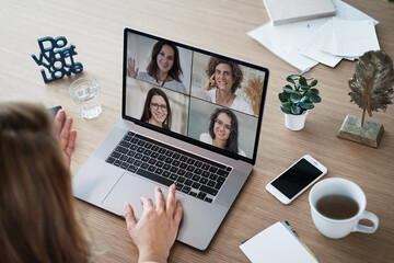 back of a remote online coaching woman sitting on her work desk infront of laptop screen at her home office joining a team meeting or women circle of 4, coaching event or watching video conference