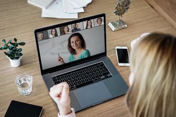 laptop on a work desk showing back view of a woman watching screen of a video conference, a...