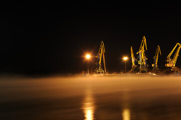 Tall harbor cranes operate in the port on an early winter morning. Port cranes for loading coal for export from Russia at the coal port hub of Murmansk, Kola Bay.