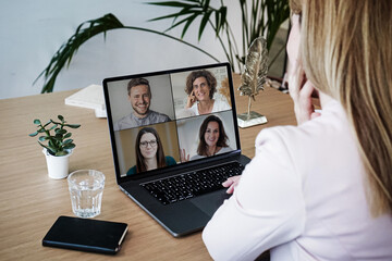 back of a remote online working business woman sitting on her work desk with laptop at her home office joining a team meeting, coaching, webinar or watching video conference 