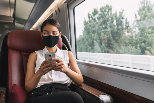 Face mask in public transport during corona virus. Elegant Asian passenger woman sitting in business class of train using mobile phone during travel.