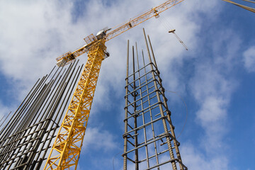 Tower construction crane and reinforcements steel bars against the blue sky. Big yellow construction crane. Close up steel construction armature.