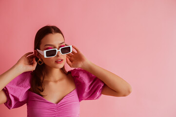 Elegant fashionable woman wearing trendy white sunglasses, pink blouse with puff sleeves, posing on pink background. Copy, empty space for text