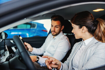 Car seller sitting in a car with a customer and showing him advantages and performances of a car.