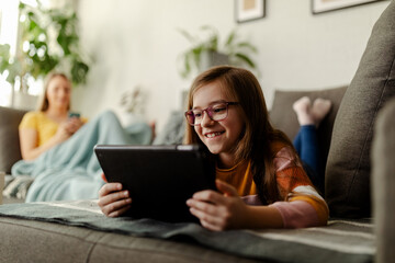 Young girl is using tablet computer while mom is in the background. Living room.