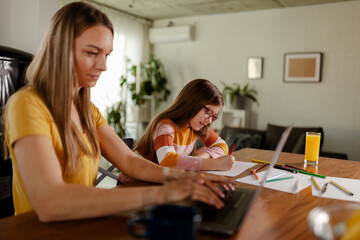 Mom and daughter are sitting together while mom is doing some job on her computer.