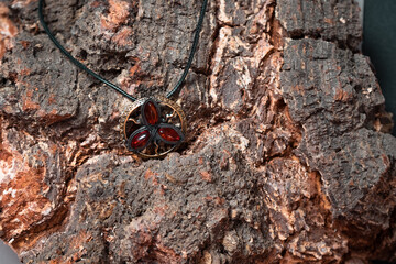 Bronze pendant in the form of a flower with amber elements close-up against the background of the tree