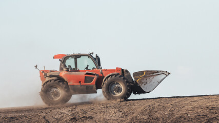 car with a bucket goes uphill through the dust