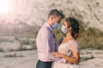Obraz premium Young loving couple in medical masks in park during quarantine on wedding day.