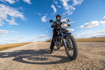 Fototapeta na wymiar man in a black uniform on bike against the backdrop of panorama of field and blue sky. motorcycle travel concept