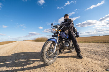 Obraz na płótnie Canvas man in a black uniform on bike against the backdrop of panorama of field and blue sky. motorcycle travel concept