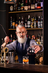 gray-haired man with a beard bartender prepares a cocktail