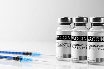 Coronavirus vaccination theme. Three vials with COVID-19 vaccine and syringes on glass laboratory white bench, close up, space for text