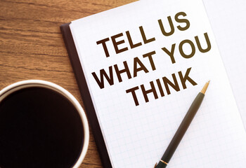 Tell Us What You Think - text on notepad on wooden desk.