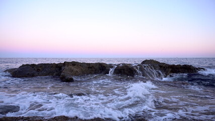 Waves on the Mediterranean Sea. Waves hit the rocks at pink sunset