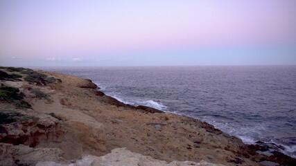 Waves on the Mediterranean Sea. Waves hit the rocks on a rocky shore. Pink sunset