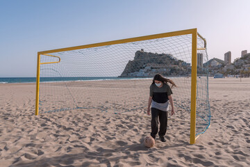 Teenager playing soccer on the beach with protective face mask. Sports.