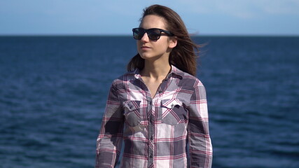 A young woman on a background of the sea. Girl in sunglasses in sunny weather. Explores the nature around