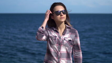 A young woman on a background of the sea. Girl in sunglasses in sunny weather. Explores the nature around