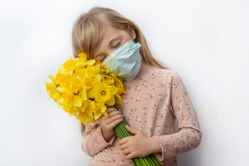 This is a blonde girl in a medical mask holding a bouquet of daffodils