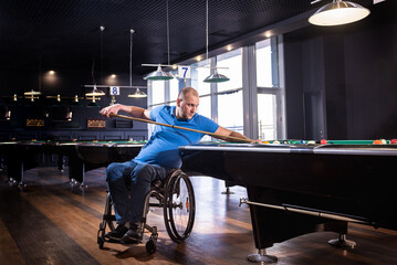 Adult man with disability in a wheelchair play billiards in the club