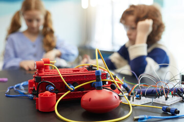 Close up of red robotic machine on table in engineering class with children in background, copy space