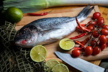 Fresh uncooked dorado or sea bream fish with lemon slices, spices, herbs and vegetables. Mediterranean cuisine. 
