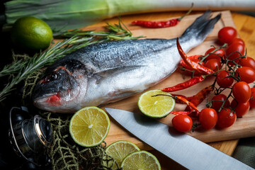 Fresh uncooked dorado or sea bream fish with lemon slices, spices, herbs and vegetables. Mediterranean cuisine. 