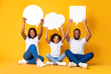 Smiling black family hoding speech bubbles at studio