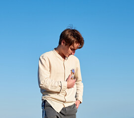 A Caucasian man wearing a beige shirt from Spain hanging his glasses from his chest pocket on clear sky background