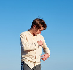 A Caucasian man wearing a beige shirt from Spain hanging his glasses from his chest pocket on clear sky background