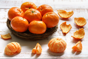 Fresh juicy pilled mandarins on wooden plate and white wooden background 