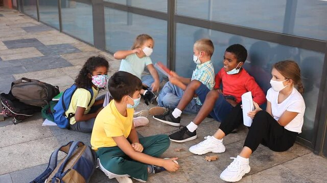 Elementary school girls and boys wearing protective face masks talking outside before lesson. High quality FullHD footage