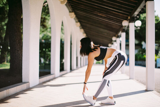 Fitness woman doing stretching legs exercise outdoors. Female runner in sportswear exercising morning routine. Slim athletic woman run workout. 
